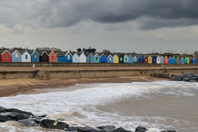 Buildings by sea against cloudy sky