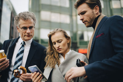 Low angle view of worried business people looking at mobile phone while standing in city