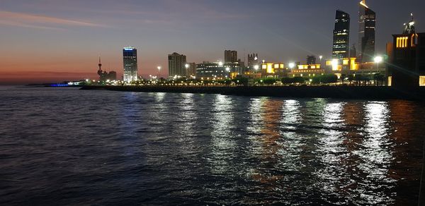 Illuminated buildings by river against sky at night