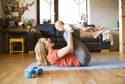 Happy mother lifting up baby at home lying on mat