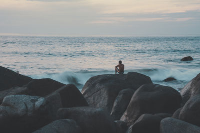 Man standing on rocks at beach against sky during sunset