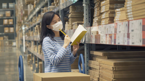 Woman holding book and pen wearing mask standing in warehouse