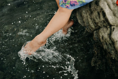 Low section of woman splashing water while sitting on rocks