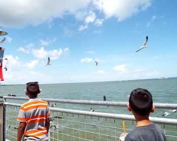 Rear view of men standing at seaside against sky