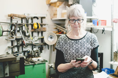 Senior woman using mobile phone in jewelry workshop