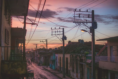 Power lines in city against sky during sunset