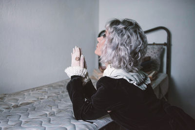 Side view of woman sitting against wall at home