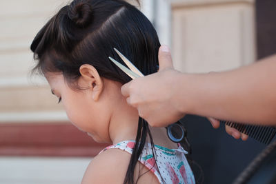 Cropped hands grooming hair of girl