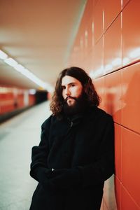 Young man looking away while standing by wall in subway station