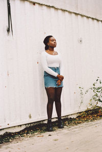 Portrait of young woman standing against wall