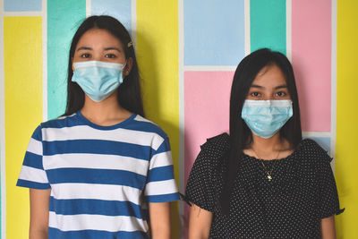 Portrait of two young woman standing against painted wall