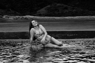 Happy woman in bikini sitting on shore at beach