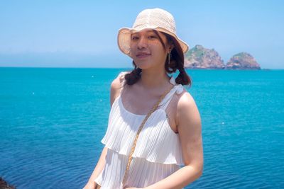 Portrait of beautiful young woman standing against blue sea