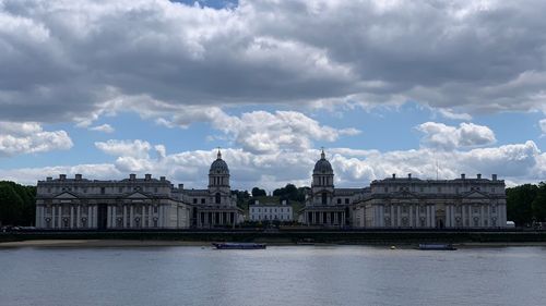 Buildings by river against cloudy sky