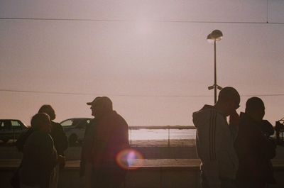 Silhouette people standing by railing against clear sky