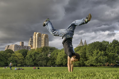 Man doing handstand on grassy field against cloudy sky