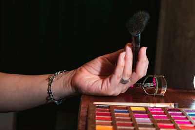 View of a girl's arm holding a makeup brush in her hand, next to her brown wooden dressing table