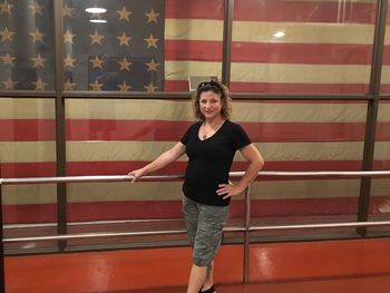 Portrait of smiling woman standing by window against american flag