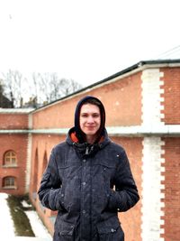 Portrait of smiling man standing against house during snowfall