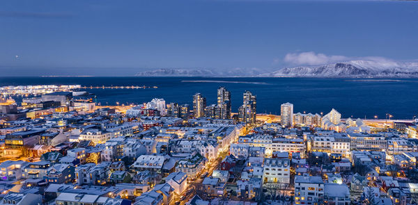 High angle view of illuminated buildings by sea against blue sky