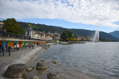 People at riverbank against cloudy sky