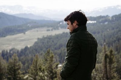 Thoughtful man wearing black jacket standing against mountains