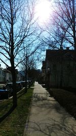 Footpath amidst bare trees and buildings against sky