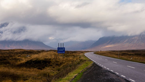 Empty country road against cloudy sky