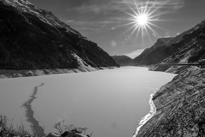 Scenic view of frozen lake amidst mountains against sky on sunny day