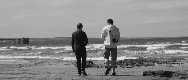 Rear view of friends walking at beach against sky