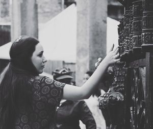 Side view of young woman standing by fence in city