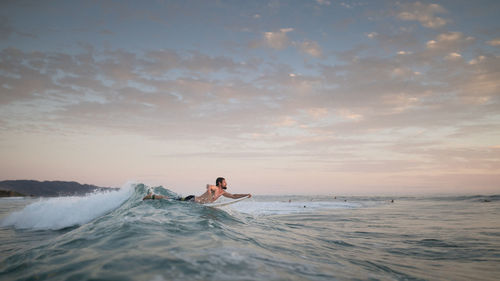 Men swimming in sea against sky during sunset