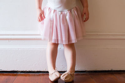 Low section of girl wearing ballet shoes against white wall