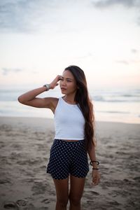 Young woman standing on beach against sky