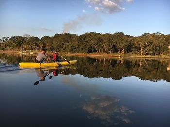 Father and son kayaking on lake against sky