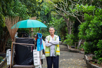 Asian man street cleaner standing with his arms crossed next to an old gabage cart 