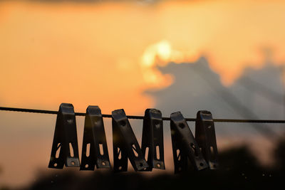 Close-up of clothespins hanging on rope against sky during sunset