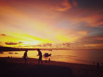 Silhouette friends standing at beach against sky during sunset