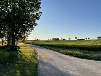 Empty road amidst field against clear sky