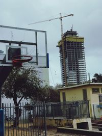 Low angle view of crane by building against sky