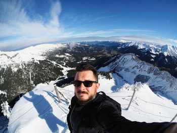 High angle portrait of man wearing sunglasses standing on snowcapped mountain