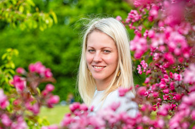 Close-up portrait of a smiling blonde woman in a blossoming garden in spring, selective focus
