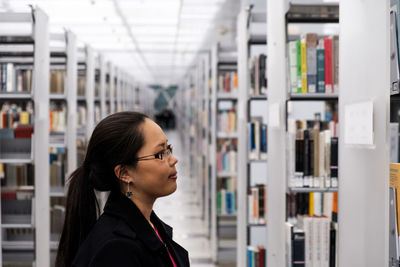 Side view of young woman looking books in shelf at library