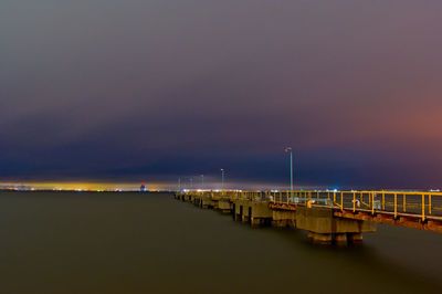 Illuminated bridge over sea against sky at night