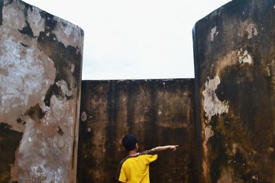 Rear view of teenage boy standing by old wall