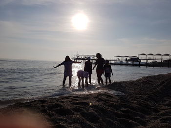 Rear view of people on beach against sky during sunset