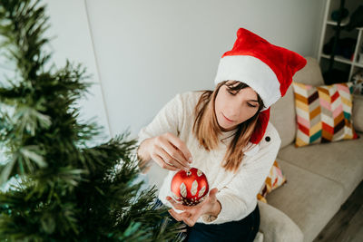 Smiling woman wearing hat decorating christmas tree at home