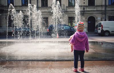 Rear view full length of girl standing against fountain in city