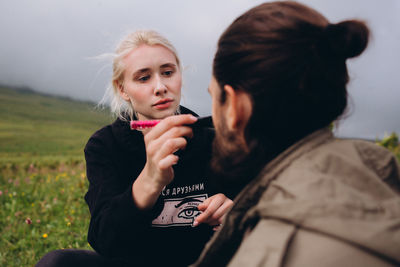 Woman applying make-up on man while sitting outdoors