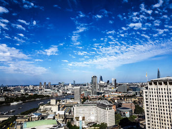 Thames river amidst cityscape against blue sky